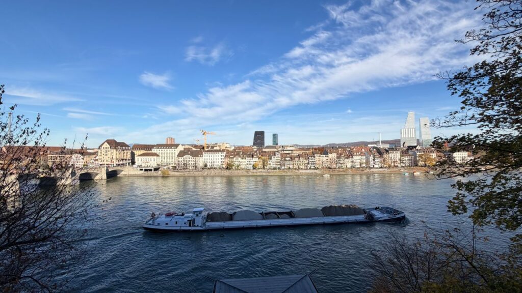 A stunning view of Basel with a boat cruising on the Rhine River under a blue sky.